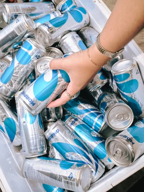 A hand reaching for a MORPHO can in a cooler filled with cans and ice